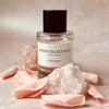 Perfume bottle labeled 'Aventurescence' by Teniqua with pink petals and crystals on a neutral background